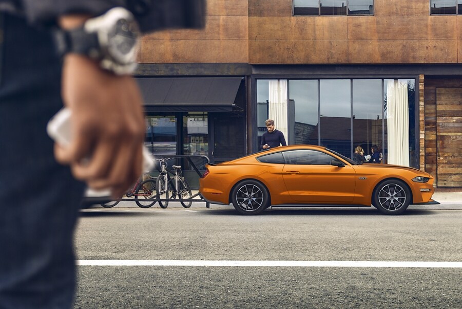 A driver approaching a 2021 Ford Mustang in Twister Orange parked on a street