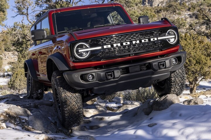 Una Ford Bronco® Wildtrak® 2023 de cuatro puertas en Race Red recorriendo un terreno escabroso y con nieve