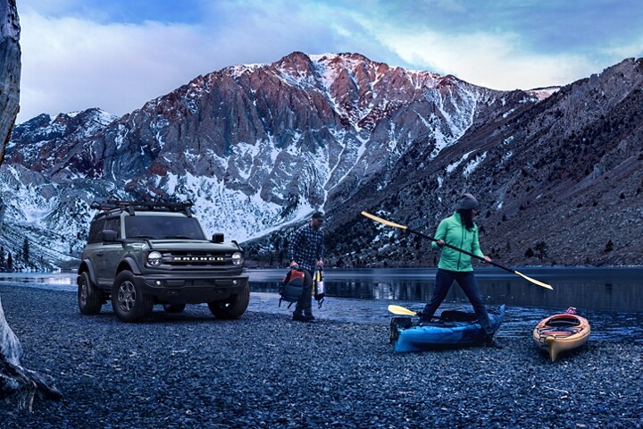 Una Ford Bronco® Big Bend® 2023 de dos puertas en Cactus Gray estacionada en la costa de un lago al pie de la montaña y personas remando
