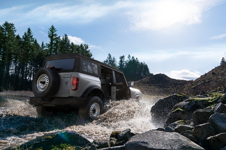 Four-door 2023 Ford Bronco® Base in Iconic Silver being driven through a stream