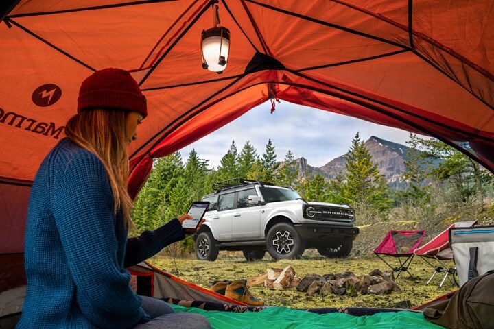 Una Ford Bronco® Outer Banks® 2023 de cuatro puertas vista a través de una carpa con una persona acampando