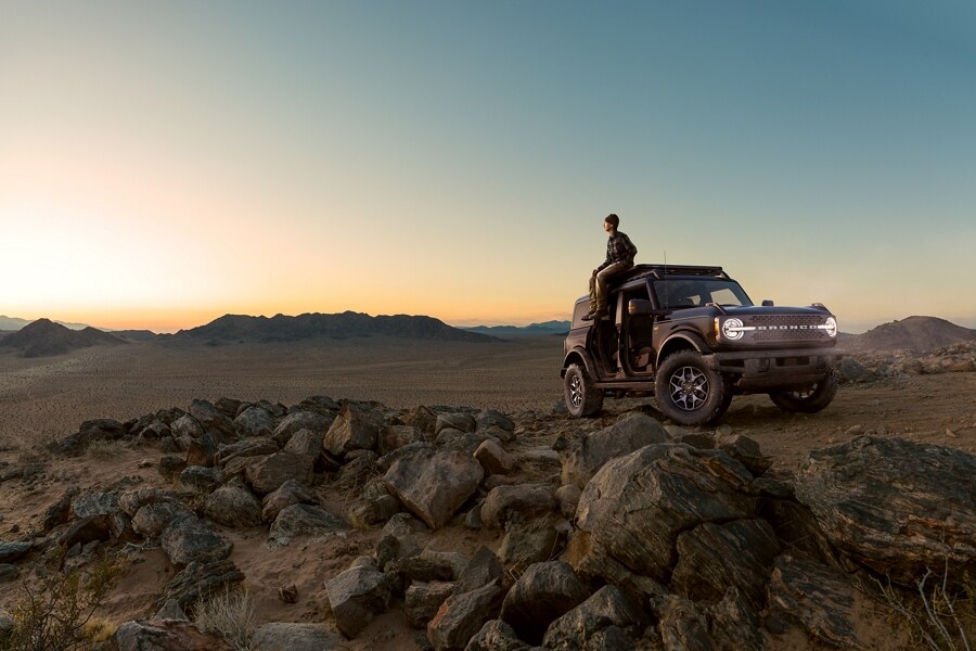 Hombre sentado en el techo de su SUV Bronco® 2023 al atardecer