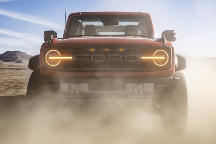 Four-door 2023 Ford Bronco® Raptor® in Hot Pepper Red being driven in the desert with top removed