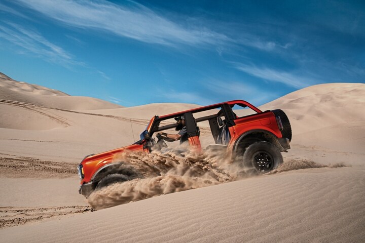Ford Bronco® Wildtrak® 2023 de cuatro puertas en Hot Pepper Red Metallic Tinted Clearcoat andando por la arena
