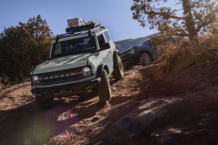 Una Ford Bronco® Black Diamond® 2023 de dos puertas en Cactus Gray andando por un camino con una Bronco® que la sigue