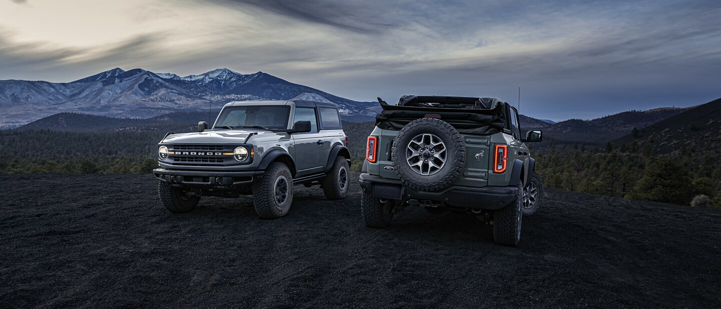 Una Bronco® 2023 de dos puertas con techo duro y Black Diamond® de cuatro puertas con techo blando al atardecer en la montaña