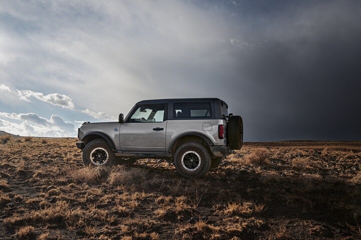 Una Ford Bronco® Badlands® 2023 en Iconic Silver andando todoterreno con techo duro de dos paneles disponible