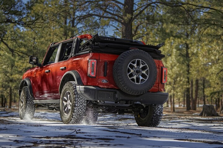 Una Ford Bronco® Badlands® 2023 de cuatro puertas en Hot Pepper Red Metallic Tinted Clearcoat andando por un bosque arenoso