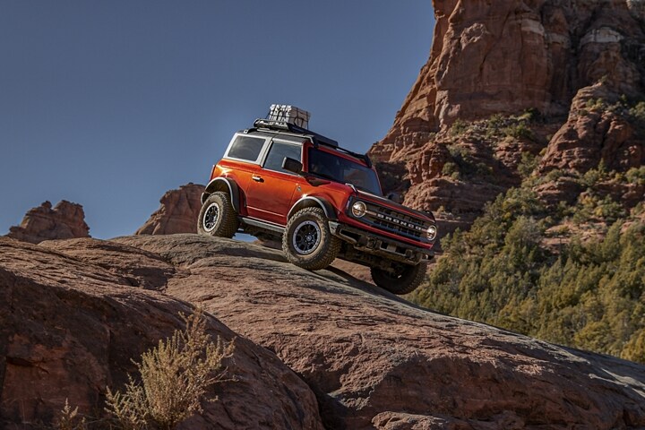 Two-door 2023 Ford Bronco® Black Diamond® in Hot Pepper Red Metallic Tinted Clearcoat with available Ford Accessories being driven on rocks