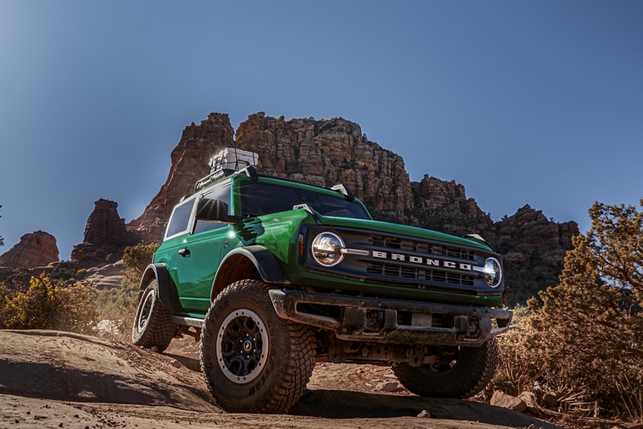 A two-door 2023 Ford Bronco® Black Diamond® in Eruption Green being driven over desert terrain