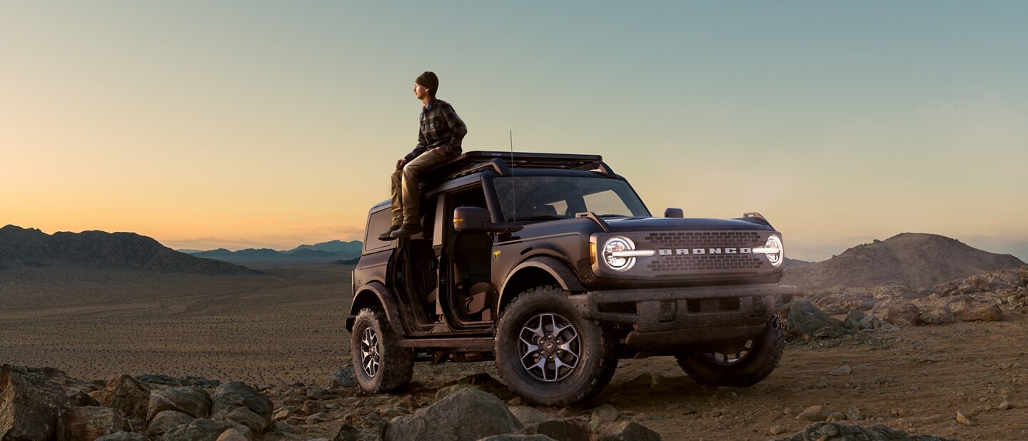 Man sitting on top of his 2024 Ford Bronco® SUV at sunset