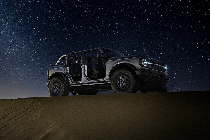 Four-door 2024 Ford Bronco® Wildtrak® in Iconic Silver with doors and roof removed parked at night