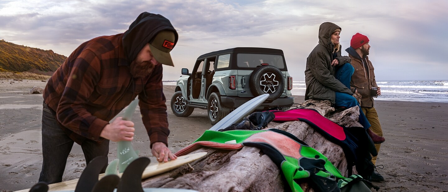 A 2024 Ford Bronco® Outer Banks® in Cactus Gray on beach with three surfers