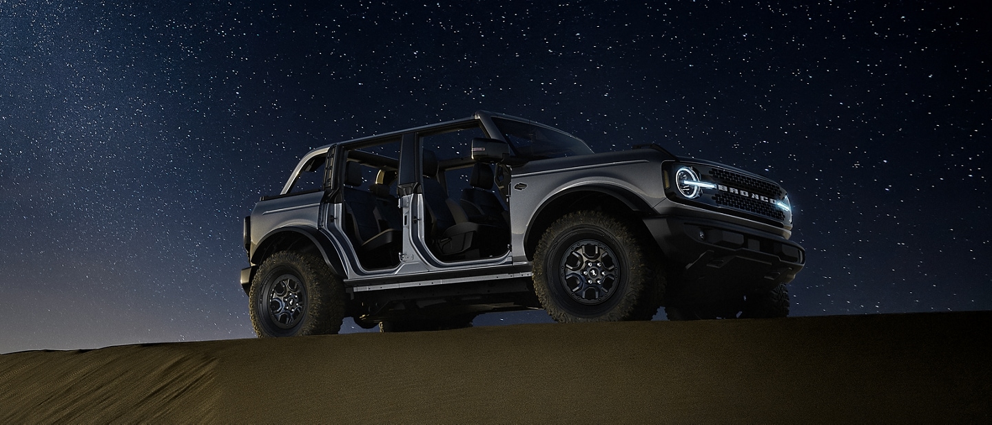 A 2024 Ford Bronco® with roof off and doors off at night atop a sand dune