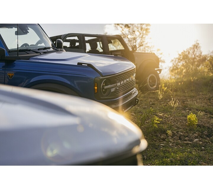 Two different 2024 Ford Bronco® SUVs with a Bronco® Sport parked at sunset