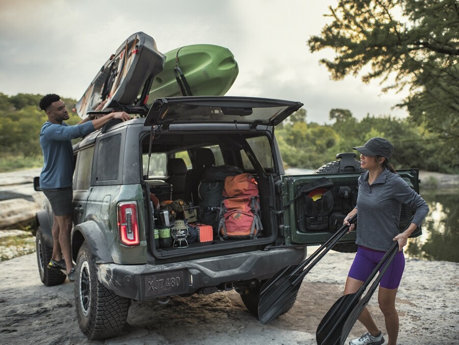 A couple removing outdoor gear from the back of their 2024 Ford Bronco® and kayaks on roof rack