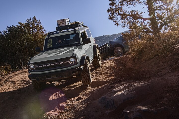 Two-door 2024 Ford Bronco® Black Diamond™ in Cactus Gray being driven on a trail with a Bronco® following