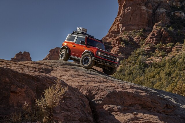 Two-door 2024 Ford Bronco® Black Diamond™ in Hot Pepper Red Metallic Tinted Clearcoat being driven down a rocky decline