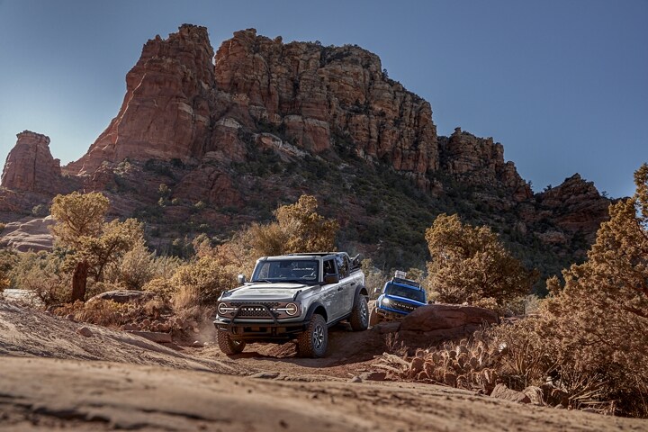 Four-door 2024 Ford Bronco® Badlands® and a two-door 2024 Ford Bronco® Black Diamond™ on a Dirt Road Being Driven Out Of Canyon