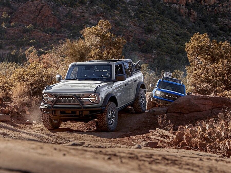 Two 2024 Ford Bronco® SUVs being driven out of a tight canyon trail