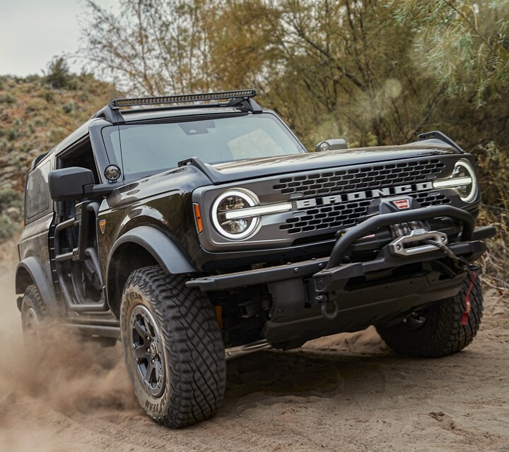 A 2024 Ford Bronco® with modular bumper and winch being driven up a dusty trail