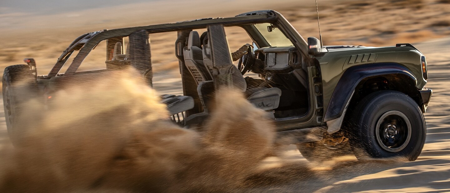 A 2024 Ford Bronco® Raptor® with top off and doors removed being driven up a sand dune