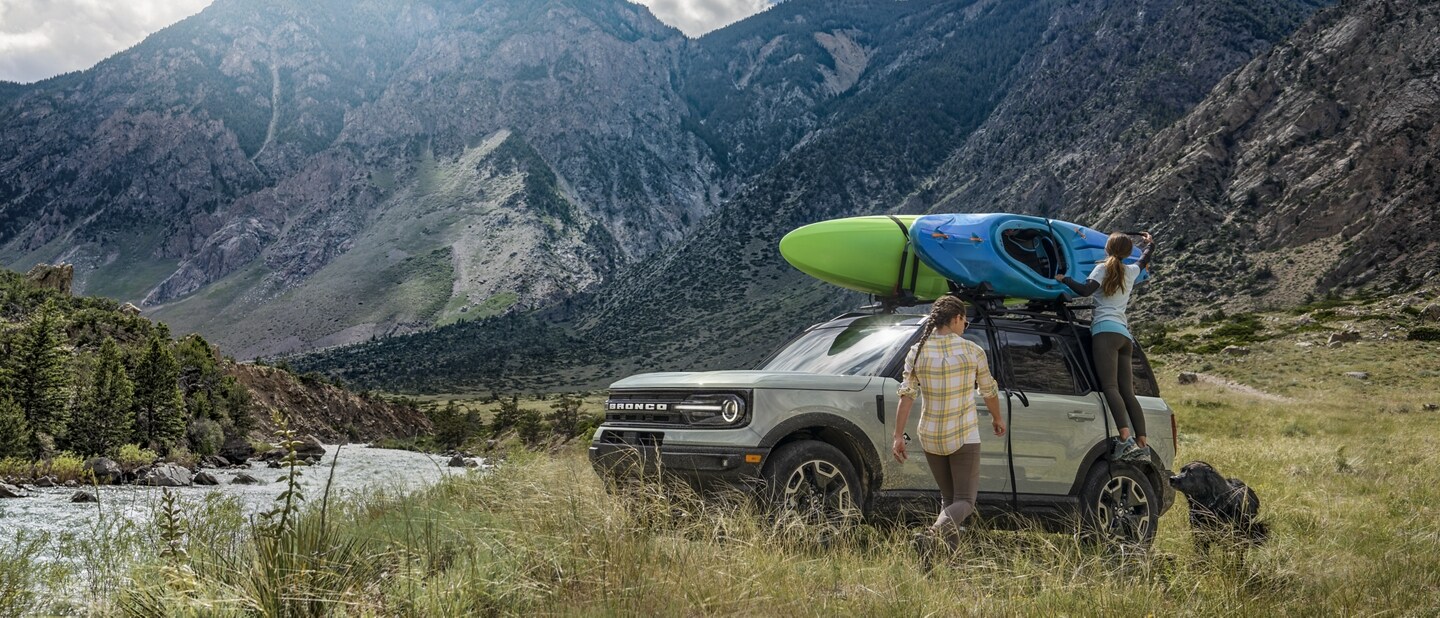 People adjusting kayaks on top of a 2021 Ford Bronco Sport parked by a river