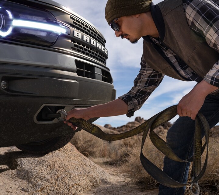 2023 Ford Bronco® Sport model with a man hooking a tow strap to the front tow hooks