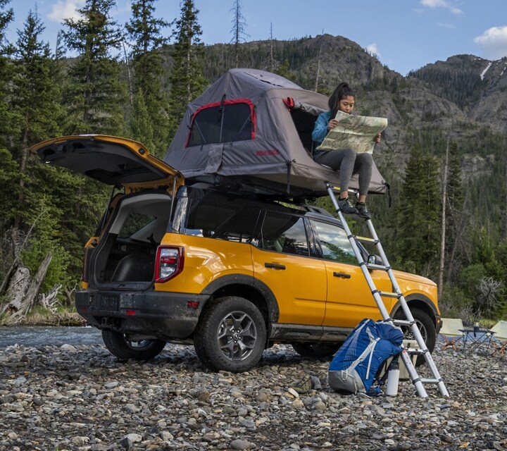 2023 Ford Bronco® Sport SUV shown with liftgate open and a woman sitting in a tent on the roof