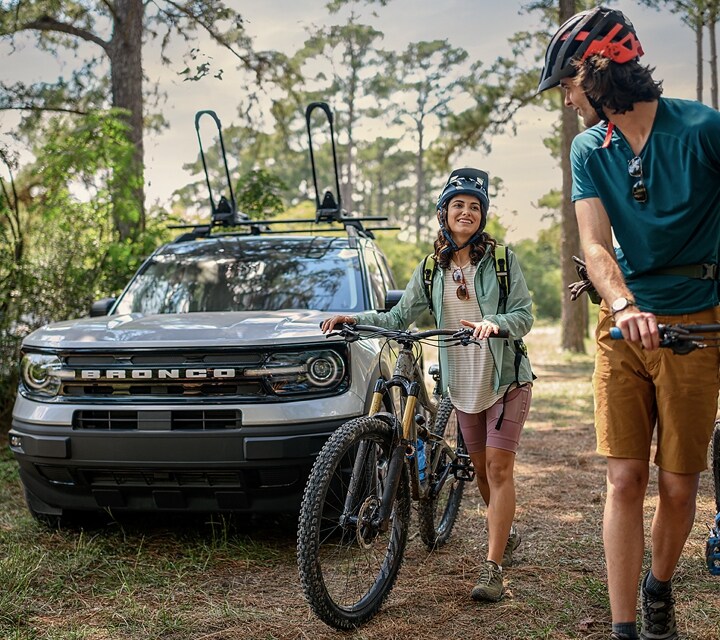 Dos personas llevando sus bicicletas a pie al lado de una Ford Bronco® Sport 2023 estacionada