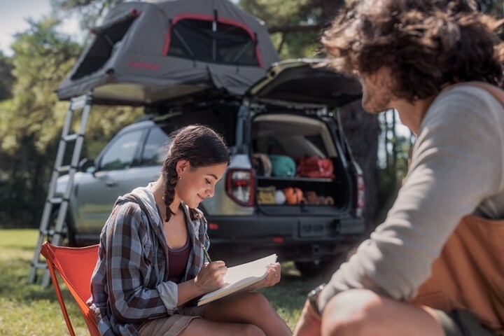 Una niña escribiendo en su diario mientras un muchacho está sentado cerca de ella y mira a la distancia