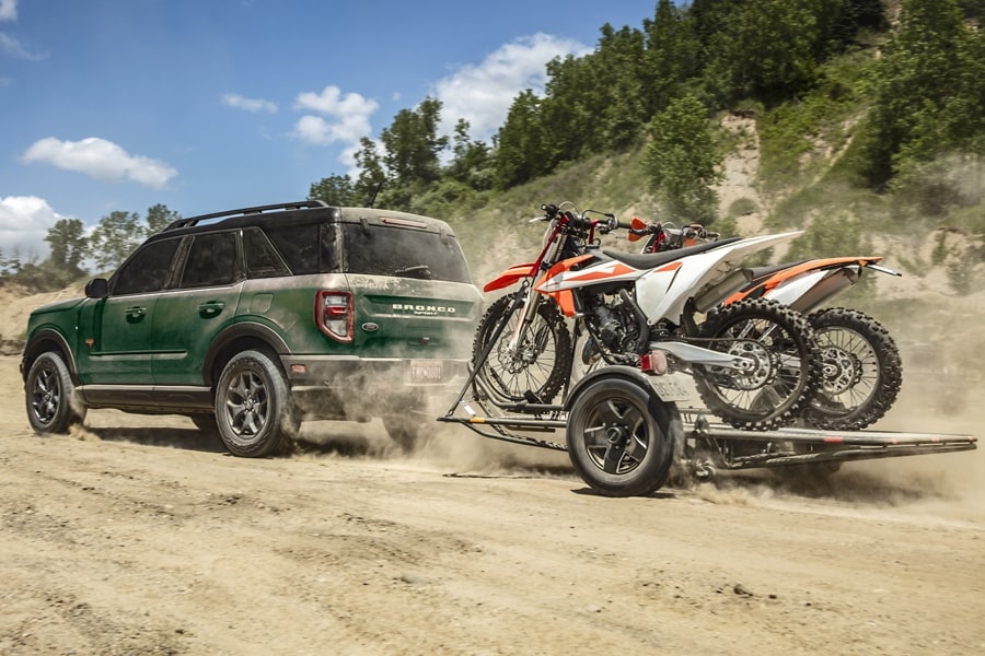 A 2024 Ford Bronco® Sport being driven, pulling a trailer with motorcycles on the back