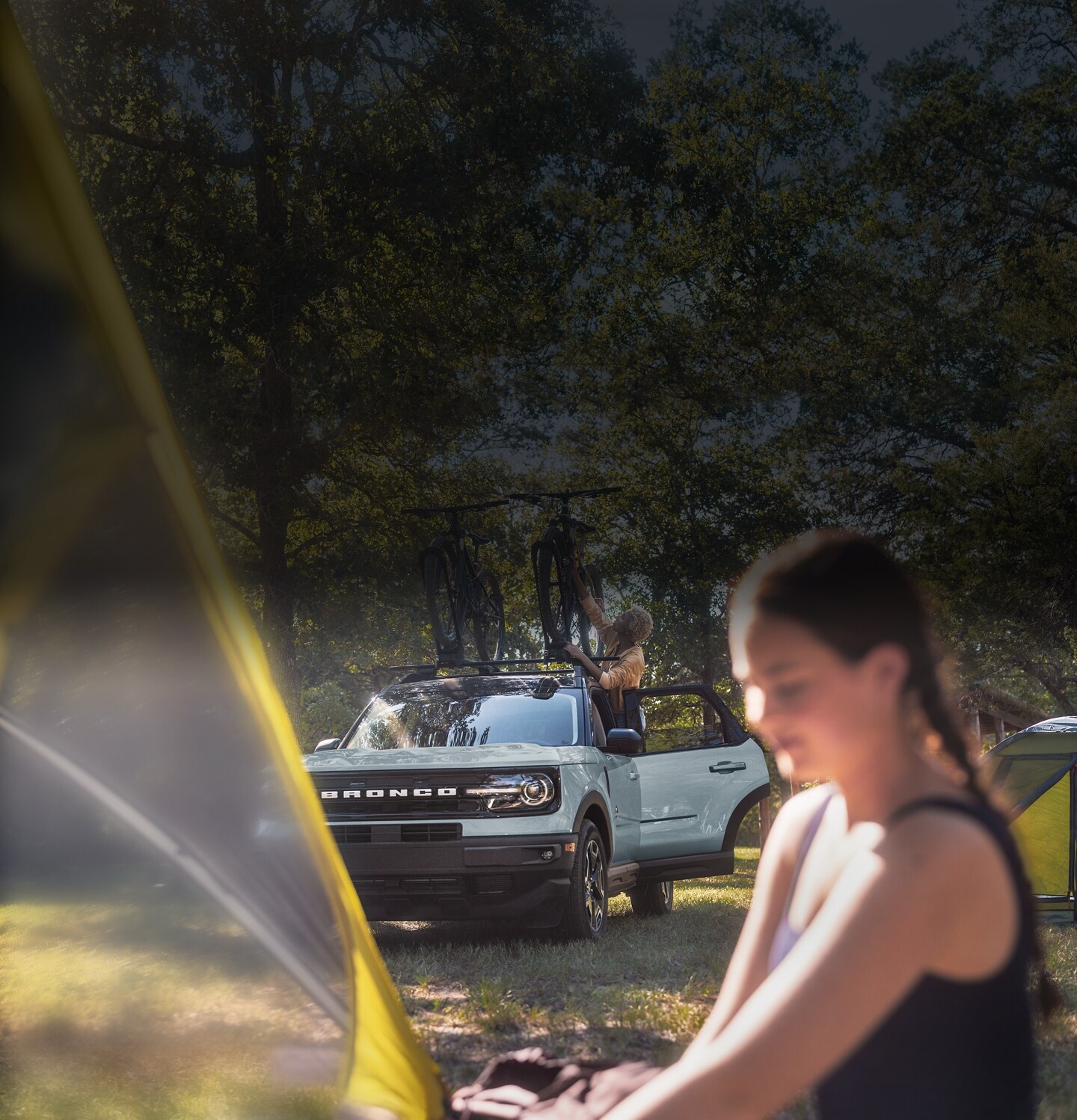 2024 Ford Bronco® Sport SUV parked on grass with a woman adjusting bike on roof with young woman standing nearby