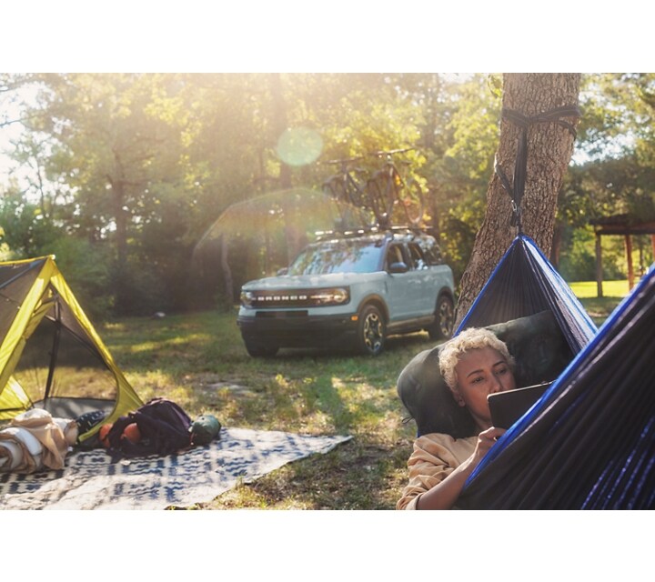 A lady lying in a hammock with gear on a blanket behind her with a 2024 Ford Bronco® Sport is in the background