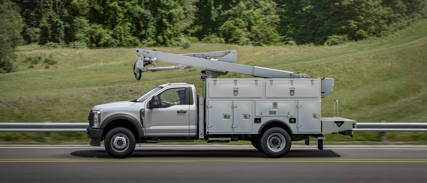 Vista lateral de la Ford Super Duty® Chassis Cab 2023 con mejoras que circula por una carretera cerca de césped y árboles