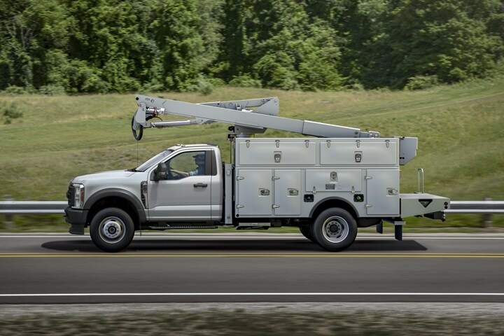 Vista lateral de la Ford Super Duty® Chassis Cab 2023 con mejoras que circula por una carretera cerca de césped y árboles