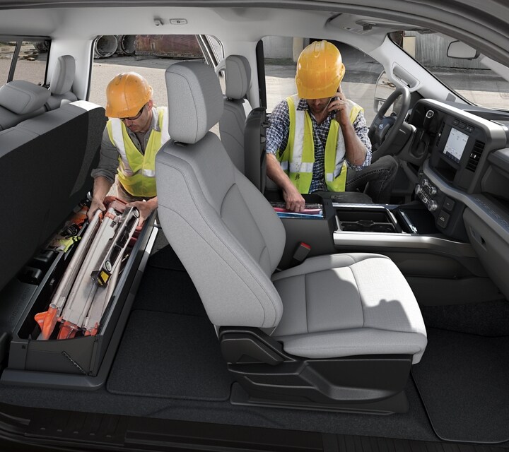 Two men in hard hats access the storage areas inside the cab of the 2023 Ford Super Duty®