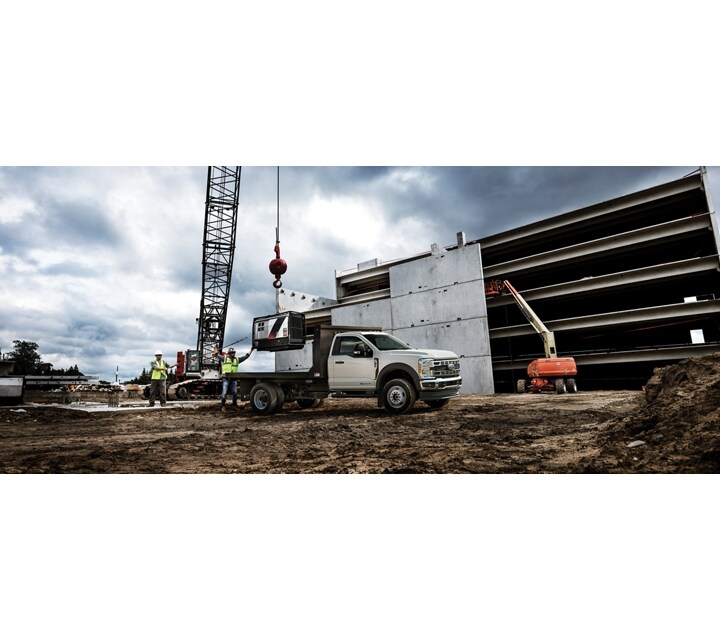 A 2024 Ford Super Duty® Chassis Cab parked on a construction site while something is being loaded onto the flat-bed