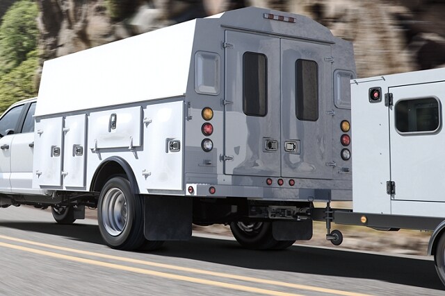 2024 Ford Super Duty® Chassis Cab with utility box upfit and trailer in tow being driven on road near trees