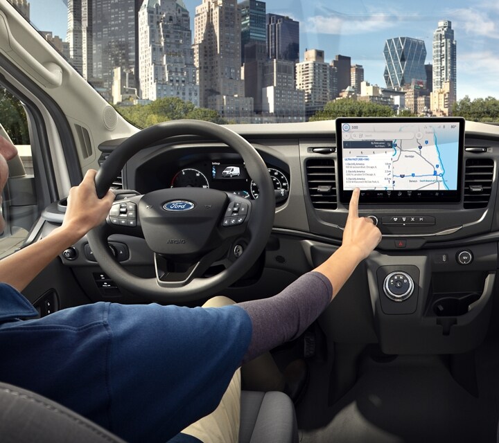 A person behind the wheel of a 2024 Ford E-Transit™ van tapping the in-vehicle display screen