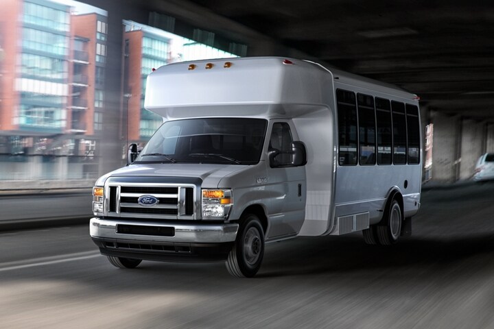 Una Ford E-Series Cutaway 2024 con ruedas traseras dobles con mejora de autobús de traslado pasando debajo de un puente
