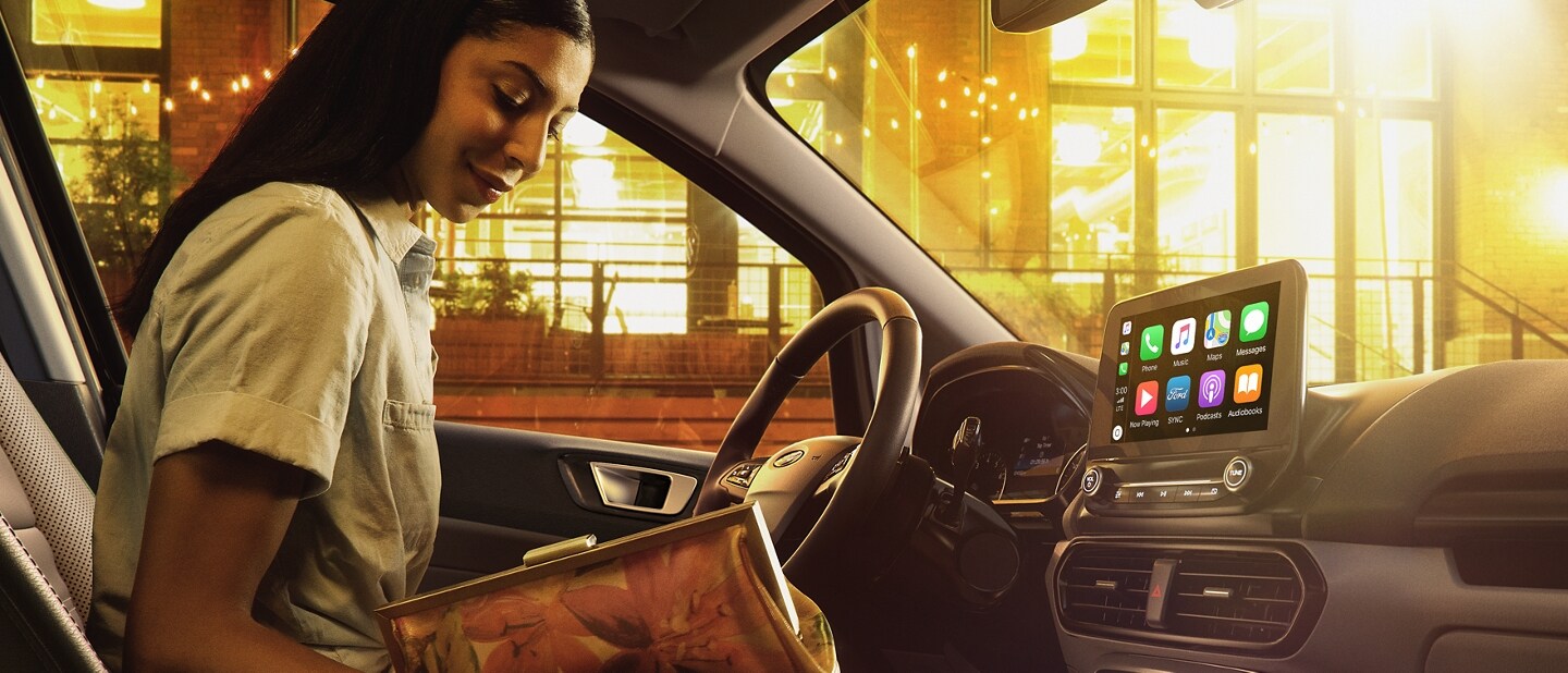 Mujer abriendo una cartera en el asiento del conductor de una Ford EcoSport 2021 con un gran edificio de fondo