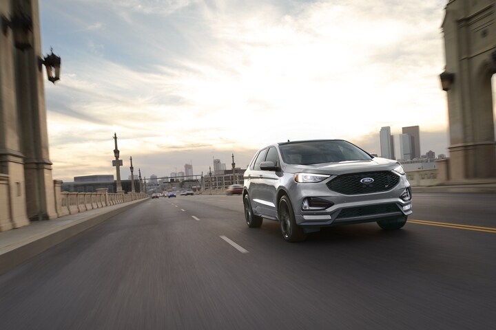Una Ford Edge 2022 andando por una carretera con una ciudad de fondo