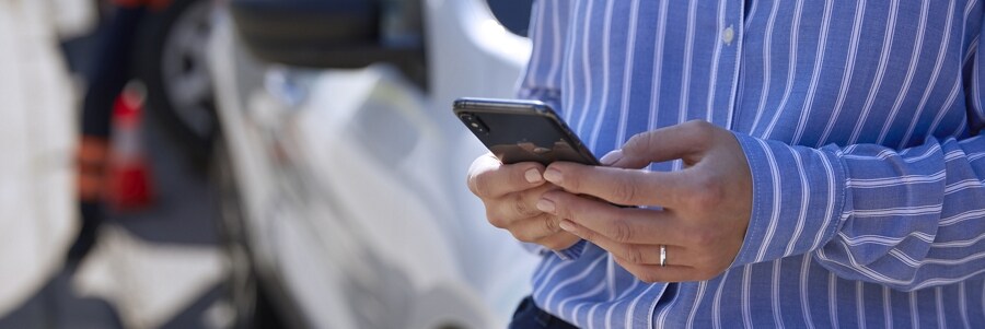 Una mujer usa un smartphone mientras está parada junto a su vehículo
