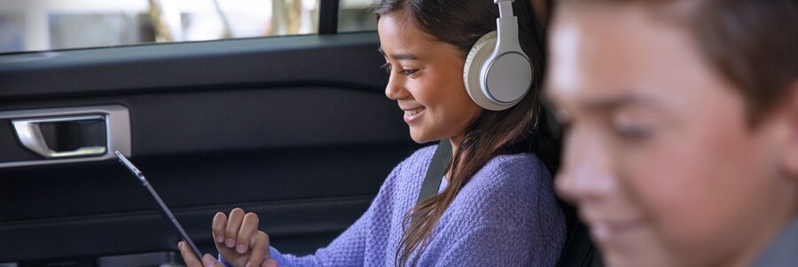 Una niña y un niño usando dispositivos con Wi-Fi en el asiento trasero de un vehículo Ford