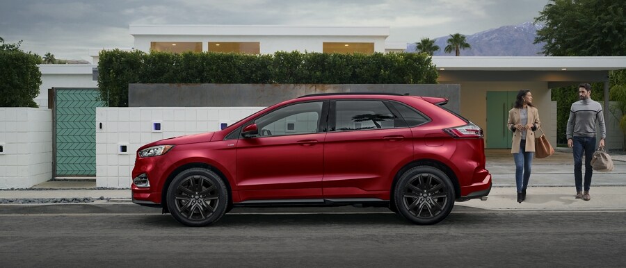 El modelo Ford Edge® ST-Line 2023 en Rapid Red estacionado frente a una casa moderna con un hombre y una mujer acercándose