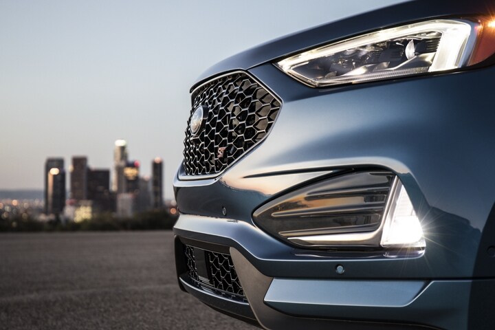 Close-up of bi-LED headlamps and fog lamps with city skyline in the background