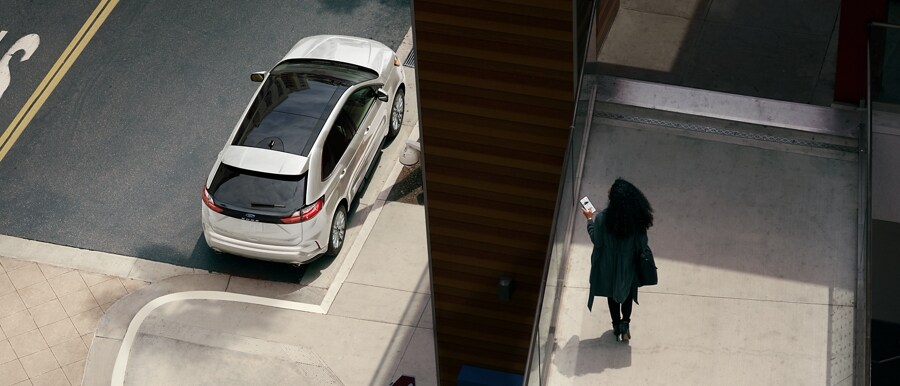 Mujer sosteniendo un smartphone en una pasarela peatonal mirando su SUV Ford Edge® 2023 estacionada en la calle abajo