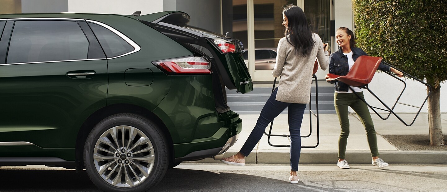 Dos mujeres con sillas se paran detrás de una Ford Edge 2023 mientras una opera la puerta trasera levadiza manos libres
