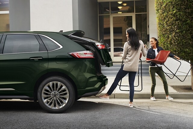 Two women holding chairs stand behind a 2023 Ford Edge as one operates the hands-free liftgate